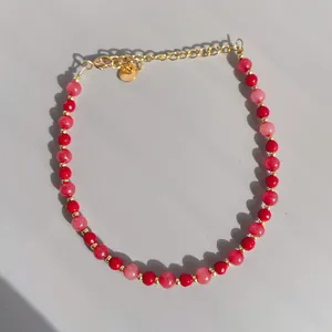 Close-up of pink and red beads with 18K gold plated steel lobster clasp and logo tag
