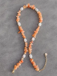 Dettaglio macro della collana boho con pietre grezze arancioni e perle bianche