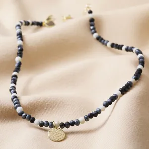 Detalle de collar de cuentas con piedras naturales y un colgante de oro martillado