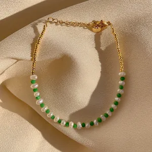 Detail of 18K gold-plated beaded bracelet with green stones and pearls on silk fabric