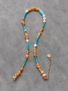 Dettaglio collana boho colorata con pietre irregolari e ciondolo a cuore in metallo