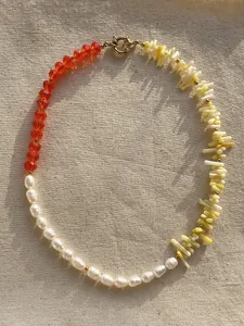 Dettaglio collana con perle, pietre arancioni e tubi gialli su sfondo di lino testurizzato