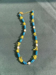 Dettaglio della collana con perline colorate, pietre gialle e perle bianche