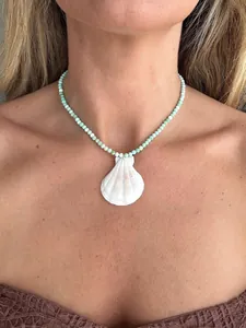 Close-up of a necklace with turquoise beads and a natural white shell pendant on a model