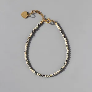 Macro view of spotted natural stone beads and gold heart pendant on a beaded bracelet
