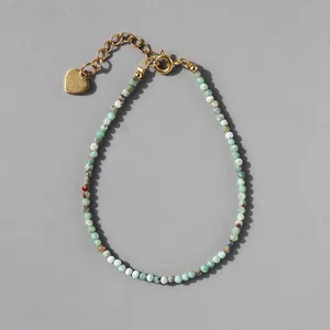 Macro shot of faceted green natural stone beads and gold heart pendant on a steel bracelet