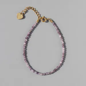 Detail of beaded bracelet with purple faceted stones, gold extender chain and heart charm