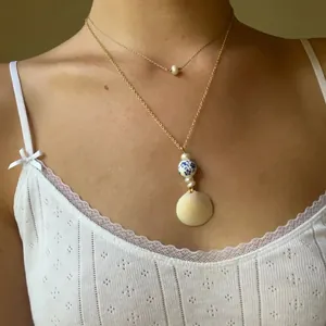 Double-layered gold necklace with blue and white porcelain beads, pearls, and shell pendant