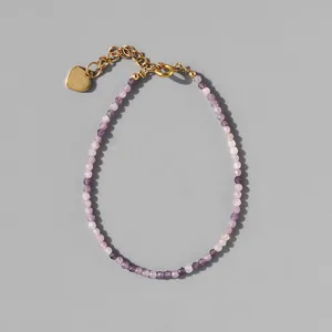 Macro detail of faceted purple natural stone beads and gold heart charm on bracelet