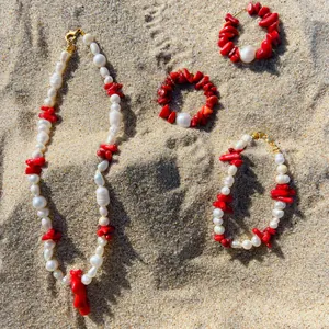 Set di gioielli con perle barocche e corallo rosso su sfondo di spiaggia dorata