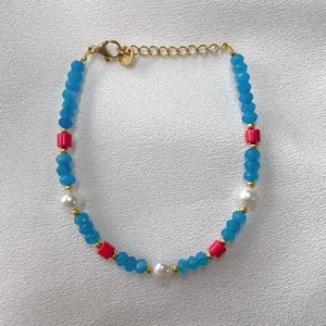 Dettaglio del bracciale con perline blu, accenti rossi e perle bianche su fondo di seta