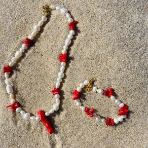 Set collana e bracciale con perle barocche e corallo rosso su sfondo di sabbia della spiaggia