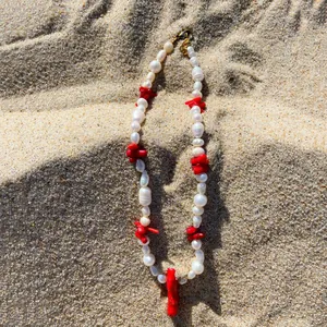 Dettaglio di perle naturali d'acqua dolce e corallo rosso su uno sfondo di sabbia