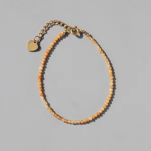 Macro shot of orange faceted beads and 18k gold heart charm on a delicate bracelet