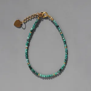 Gros plan de perles vertes à facettes avec un pendentif cœur doré sur un bracelet boho