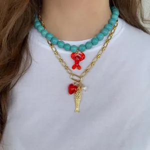 Collier superposé avec perles turquoise, pendentif homard rouge et breloques dorées sur t-shirt