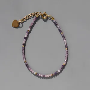 Détail d'un bracelet en perles violettes avec un pendentif cœur doré et fermoir