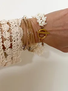 Dettaglio di bracciali dorati bohémien e bracciale di perle bianche con chiusura a T in oro