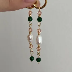 Orecchini pendenti con perle barocche, cristalli colorati e anelli dorati su sfondo grigio