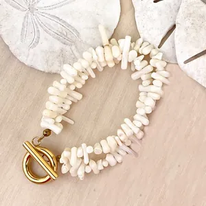 Dettaglio di collana in perle naturali con chiusura OT dorata su fondo in legno