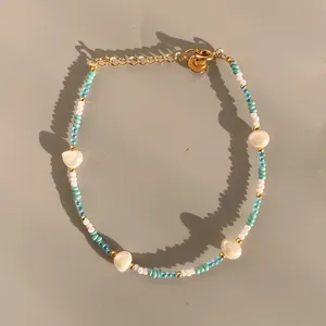 Dettaglio di bracciale con perline colorate, catena dorata, perle bianche e tocchi menta