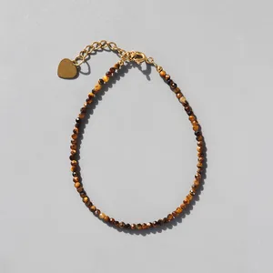 Detail of faceted tiger eye beaded bracelet with 18k gold heart charm and chain