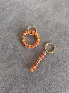 Detailed macro view of asymmetric orange natural stone beaded earrings in gold finish