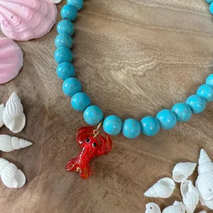 Collier de perles turquoise avec un pendentif homard rouge sur fond en bois