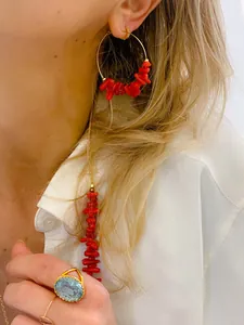 Primo piano di orecchini a cerchio in corallo rosso e anello con gemma blu su modella