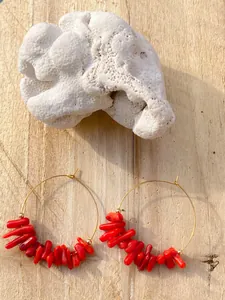 Dettaglio di orecchini a cerchio dorati con perle di corallo rosso su fondo in legno rustico