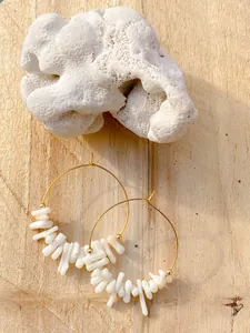 Dettaglio di orecchini a cerchio dorati con perle di pietra naturale bianca su corallo