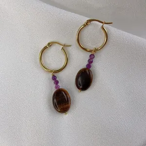 Detail of gold hoop earrings with purple beads and tiger eye stone on white silk background