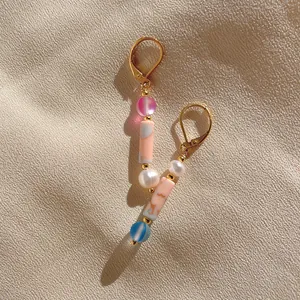 Close-up of asymmetric long drop earrings with mixed natural stones and gold hooks
