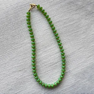 Detalle de collar de cuentas verdes con cierre de palanca dorado sobre fondo de lino