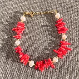 Dettaglio della collana con pietre corallo rosse irregolari e perle d'acqua dolce bianche