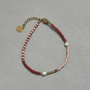Close-up of beaded bracelet with red pearls and a gold heart pendant on grey leather