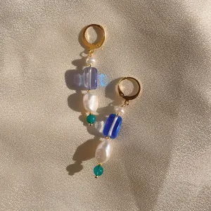 Detail of beaded drop earring with baroque pearl and colorful stones on champagne fabric