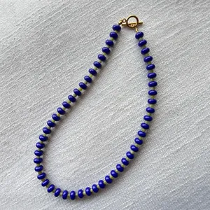 Detalle macro de collar bohemio con cuentas azules y cierre de barra en metal dorado