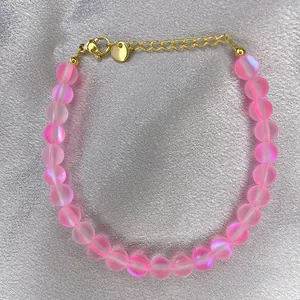 Dettaglio del bracciale con perline opache iridescenti e chiusura dorata su seta