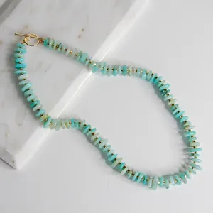 Detalle de collar de cuentas turquesas con cierre de barra dorado sobre mármol
