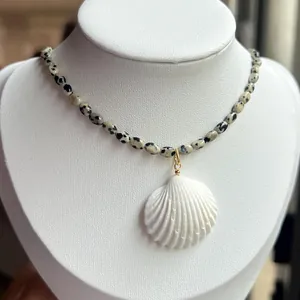 Dalmatian stone beaded necklace with white shell pendant on a jewelry display
