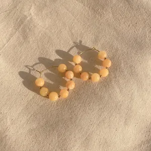 Detail of colorful beads on gold hoop earrings over a textured beige linen background