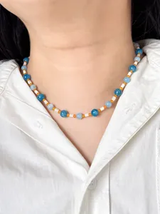 Blue and orange stone beaded necklace with white shell accents worn on a white shirt