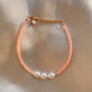 Macro detail of orange beaded bracelet with baroque pearls on champagne satin background