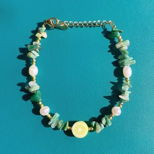 Dettaglio del bracciale con pietre colorate, ciondolo a limone e perla su pelle blu