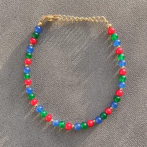 Detail of handmade beaded bracelet with red, green, blue stones and gold lobster clasp
