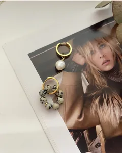 Close-up of asymmetric gold hoop earrings with baroque pearl and spotted marble stone