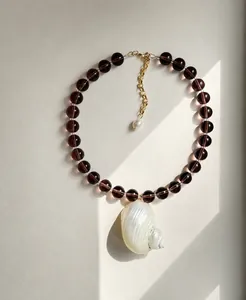 Detail van de paarse kralenketting met een grote natuurlijke spiraalvormige schelphanger