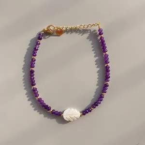 Macro detail of beaded bracelet with purple gemstones, shell leaf pendant and gold clasp
