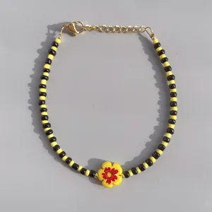 Macro shot of yellow and black glass beaded bracelet with red flower charm and golden clasp